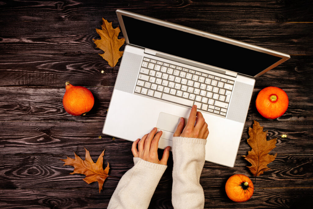Autumn pumpkins on wooden background with hands using a laptop computer from above