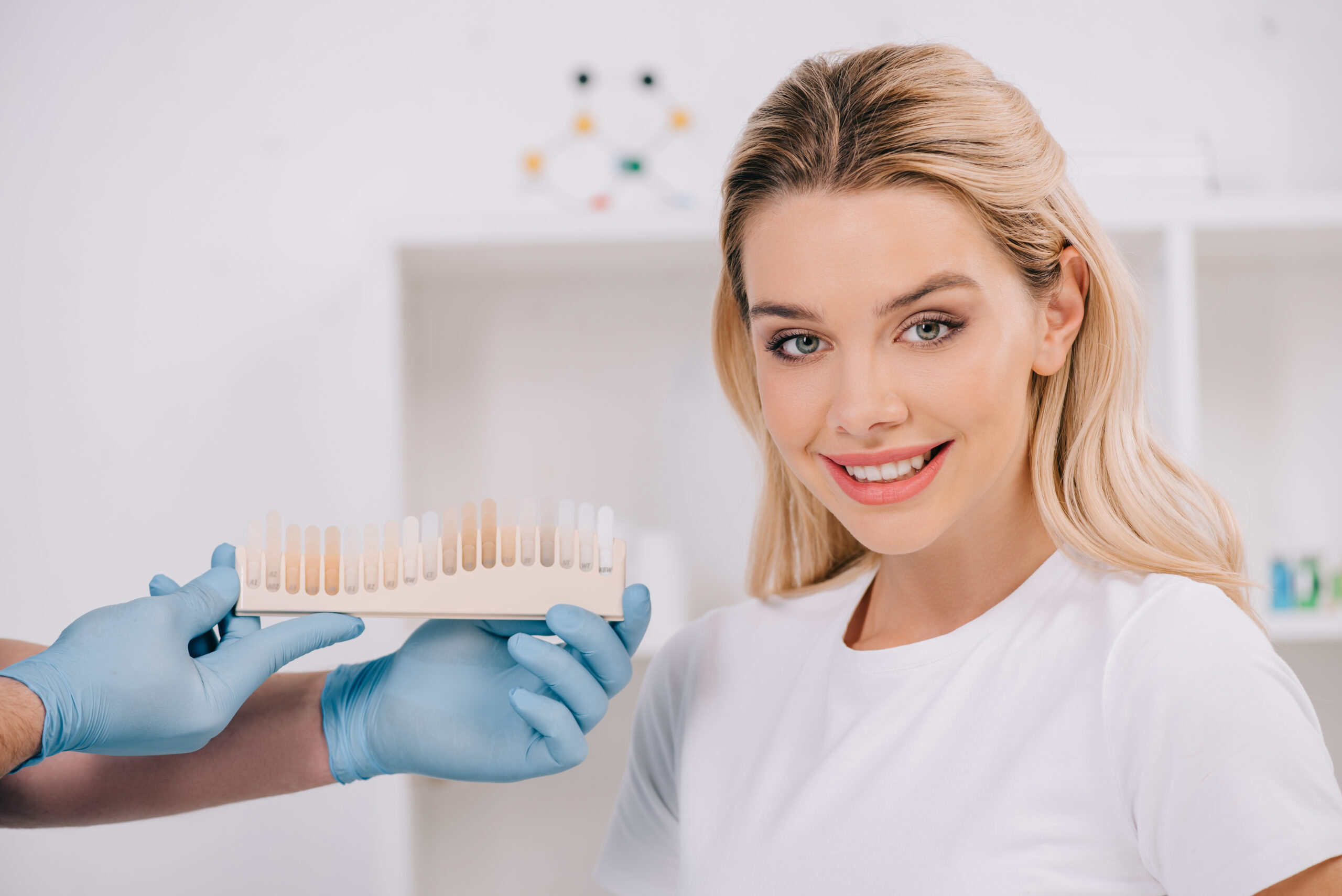male dentist holding teeth color palette while beautiful smiling woman looking at camera in clinic