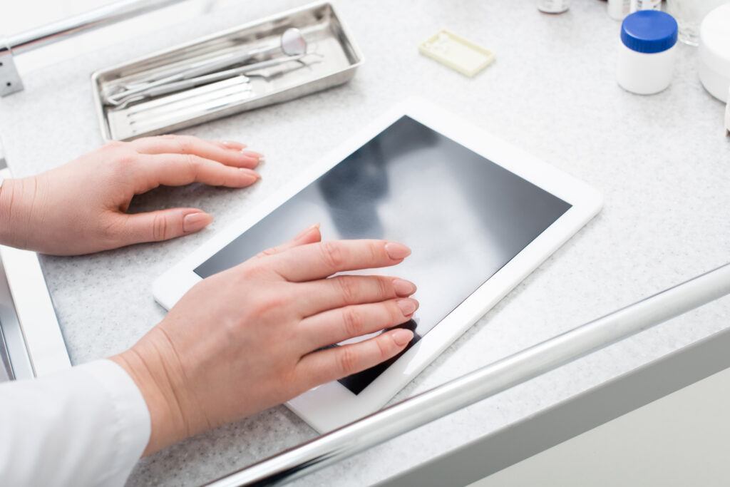 partial crop view of female hands typing on tablet with blank screen near dental equipment on medical table